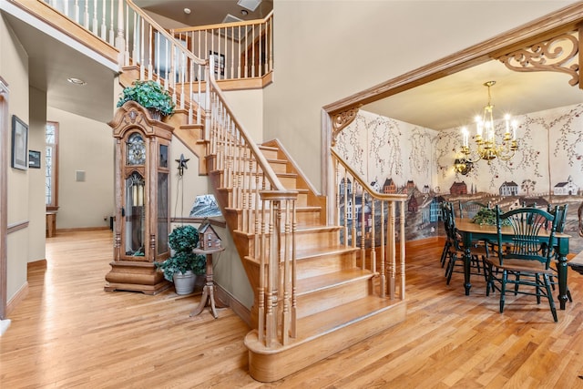 stairway featuring a towering ceiling, baseboards, a chandelier, and wood finished floors