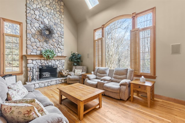 living area with high vaulted ceiling, a stone fireplace, a skylight, and wood finished floors