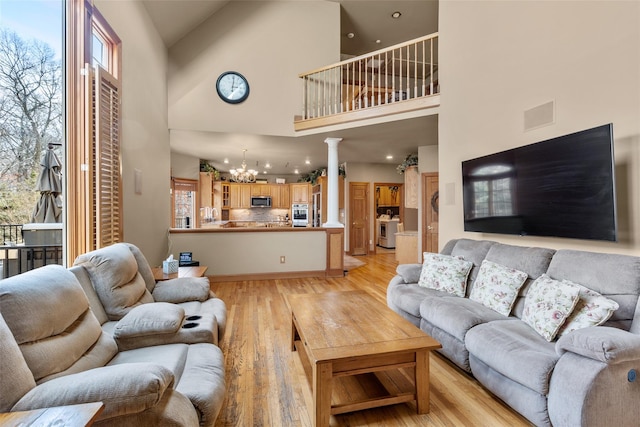 living area featuring a towering ceiling, light wood finished floors, a chandelier, and ornate columns