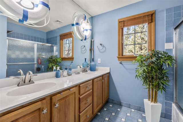 bathroom featuring a tile shower, double vanity, a sink, and visible vents