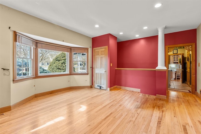 unfurnished room with ornate columns, baseboards, and wood finished floors