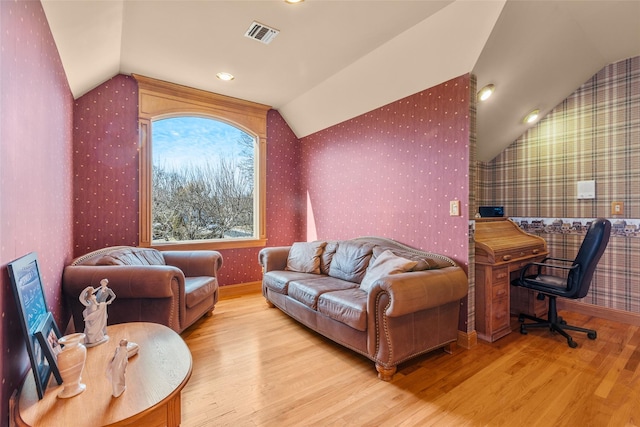 living room with visible vents, vaulted ceiling, and wallpapered walls