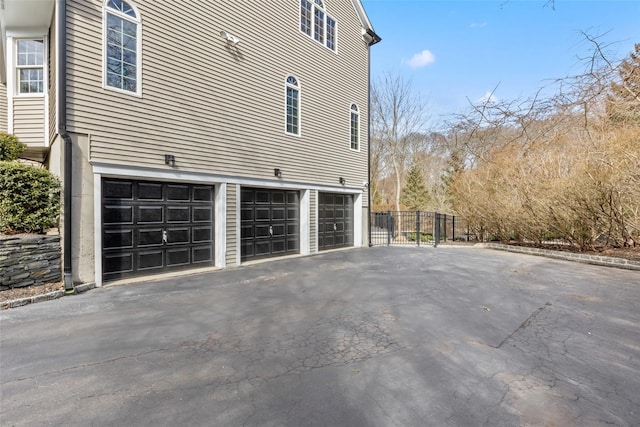 view of side of home featuring driveway, an attached garage, and fence