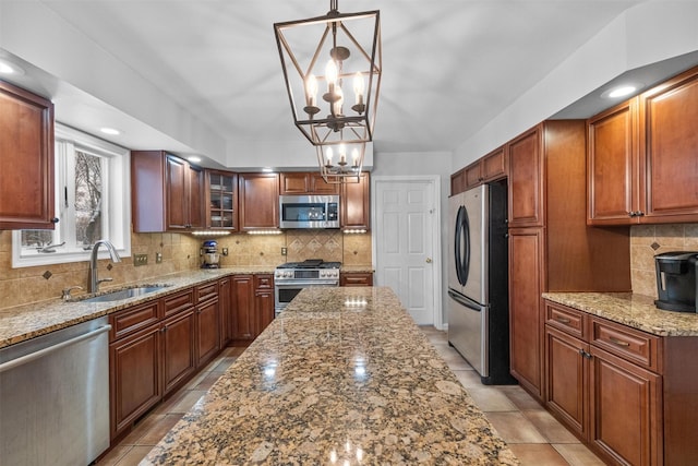 kitchen featuring sink, pendant lighting, stainless steel appliances, light stone countertops, and decorative backsplash