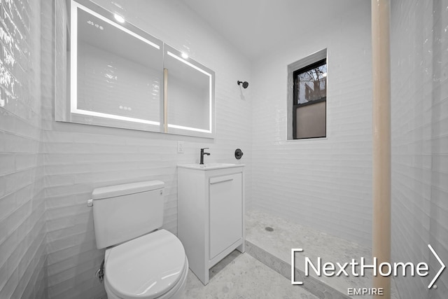 bathroom with tiled shower, vanity, toilet, and tile walls