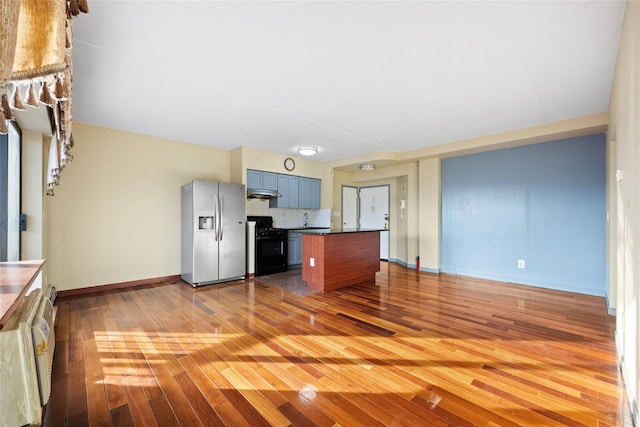 kitchen with blue cabinets, stainless steel fridge, decorative backsplash, light hardwood / wood-style floors, and gas stove