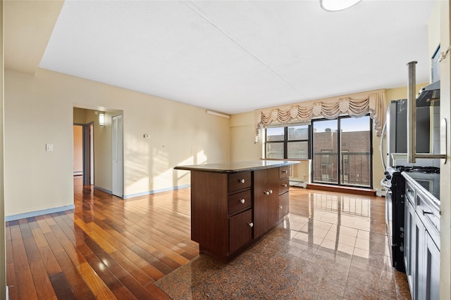 kitchen with a kitchen island, dark hardwood / wood-style floors, a baseboard heating unit, dark brown cabinetry, and gas range