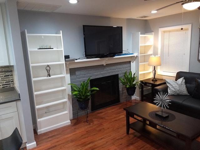 living room featuring a brick fireplace and wood-type flooring