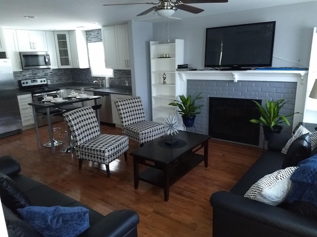 living room featuring dark hardwood / wood-style flooring, ceiling fan, sink, and a brick fireplace