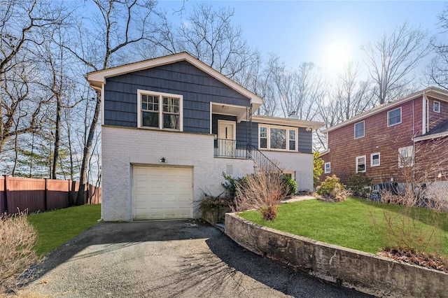 tri-level home with a front yard, fence, an attached garage, aphalt driveway, and brick siding