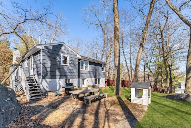 back of house featuring an outbuilding, fence, stairway, a yard, and a chimney