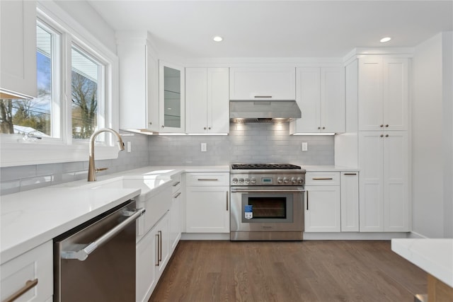 kitchen featuring dark wood-type flooring, wall chimney exhaust hood, stainless steel appliances, white cabinets, and decorative backsplash