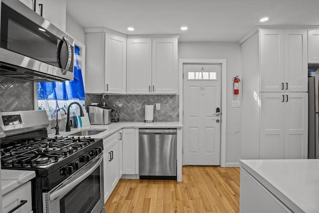 kitchen with white cabinetry, stainless steel appliances, sink, and light hardwood / wood-style floors