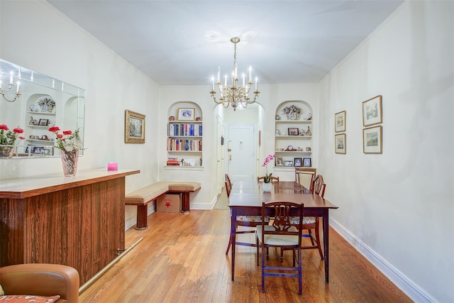 dining space with an inviting chandelier, ornamental molding, built in features, and light hardwood / wood-style floors