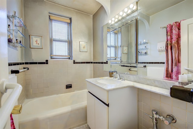 bathroom featuring vanity, a tub to relax in, plenty of natural light, and tile walls