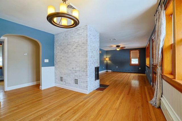 empty room with brick wall, a baseboard heating unit, ceiling fan, a brick fireplace, and light hardwood / wood-style flooring