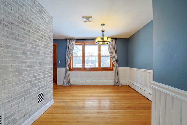 empty room with an inviting chandelier, light hardwood / wood-style flooring, and brick wall