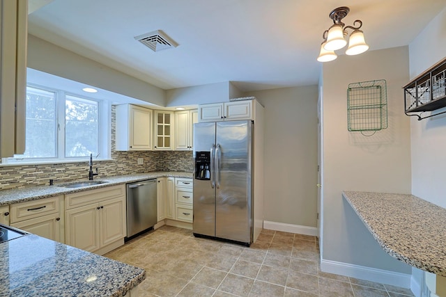 kitchen with sink, light stone counters, appliances with stainless steel finishes, decorative backsplash, and cream cabinetry