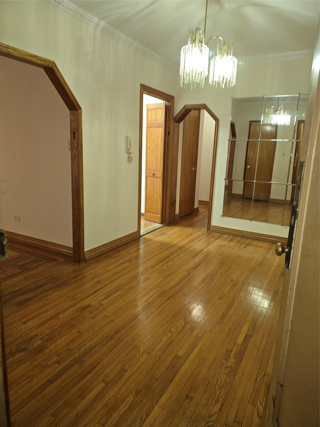 empty room featuring arched walkways, ornamental molding, wood-type flooring, and a chandelier