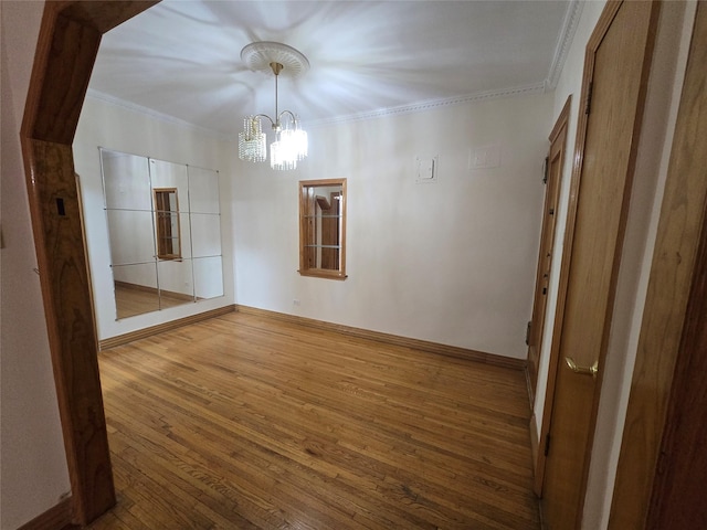 empty room with baseboards, crown molding, an inviting chandelier, and wood finished floors