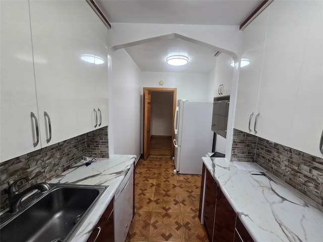 kitchen with arched walkways, white appliances, a sink, and white cabinets