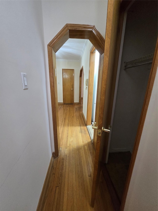 corridor with arched walkways, baseboards, and hardwood / wood-style flooring