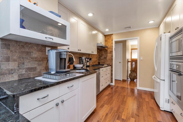 kitchen with dark stone countertops, stainless steel appliances, tasteful backsplash, white cabinets, and light wood-type flooring