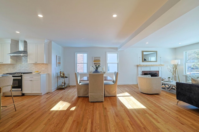 kitchen with white cabinets, stainless steel range with gas cooktop, light wood-type flooring, and wall chimney range hood