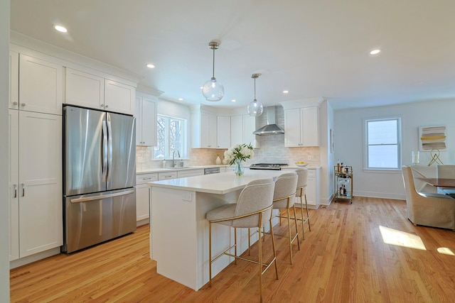 kitchen featuring decorative light fixtures, a center island, white cabinets, stainless steel appliances, and wall chimney range hood