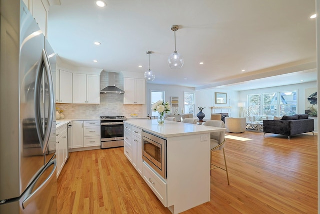 kitchen featuring a breakfast bar, white cabinets, hanging light fixtures, stainless steel appliances, and wall chimney range hood