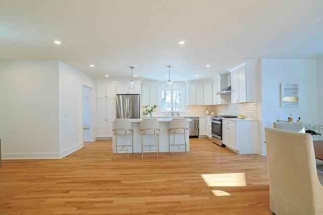 kitchen featuring white cabinets, hanging light fixtures, a center island, stainless steel appliances, and light wood-type flooring