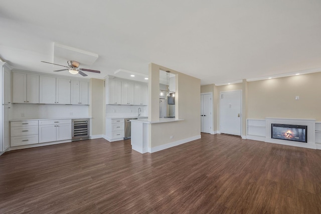 unfurnished living room with wine cooler, ceiling fan, dark hardwood / wood-style floors, and sink