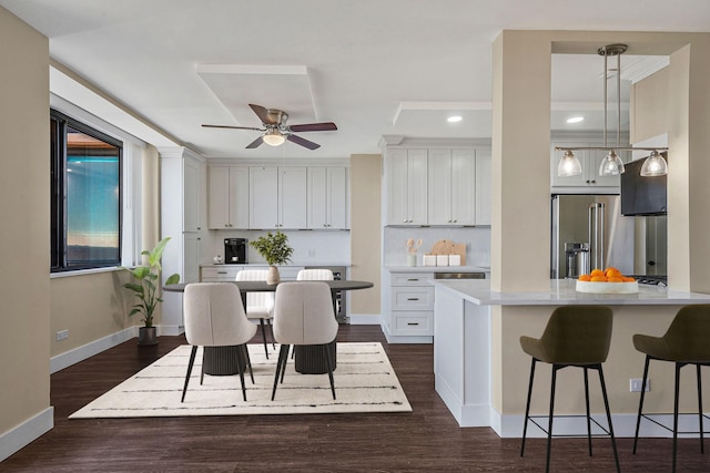 kitchen featuring dark wood-type flooring, a breakfast bar area, high end refrigerator, pendant lighting, and white cabinets