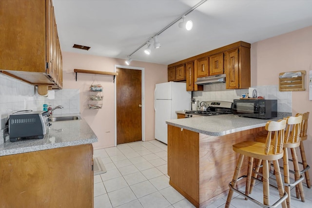 kitchen featuring sink, stainless steel stove, a kitchen breakfast bar, white refrigerator, and kitchen peninsula