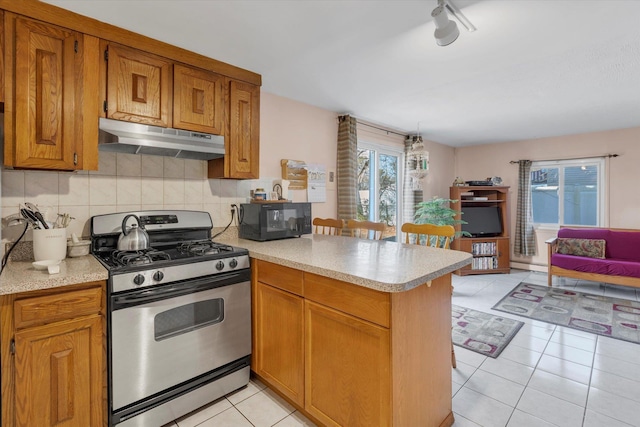 kitchen featuring stainless steel gas range, tasteful backsplash, light tile patterned floors, a baseboard radiator, and kitchen peninsula