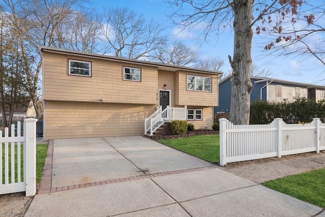 raised ranch featuring a fenced front yard, concrete driveway, and a front yard