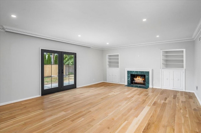 unfurnished living room featuring built in shelves, light wood-type flooring, a high end fireplace, and french doors