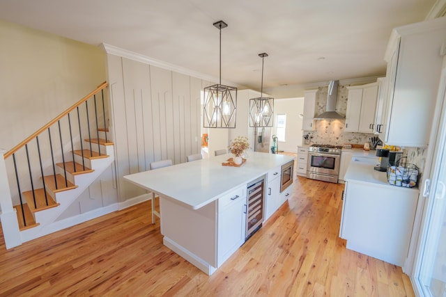 kitchen featuring wall chimney range hood, hanging light fixtures, stainless steel appliances, wine cooler, and white cabinets