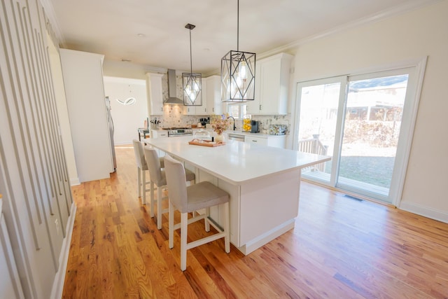 kitchen featuring hanging light fixtures, a center island, white cabinets, and wall chimney exhaust hood