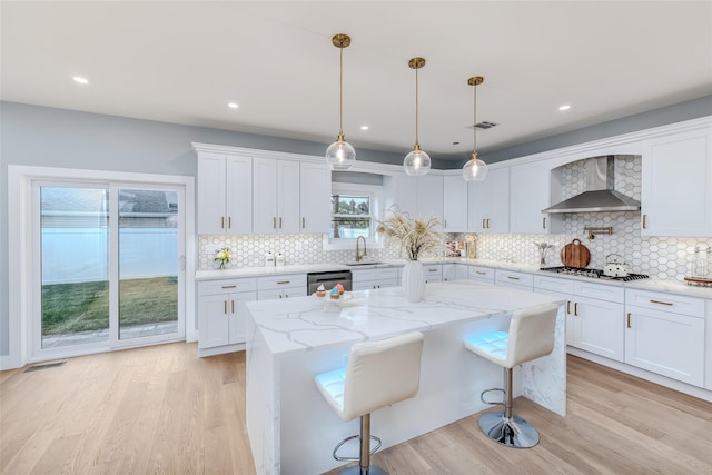 kitchen featuring a kitchen island, appliances with stainless steel finishes, white cabinetry, light stone counters, and wall chimney exhaust hood