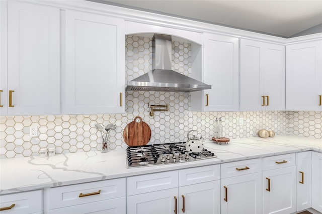 kitchen featuring wall chimney exhaust hood, white cabinetry, tasteful backsplash, stainless steel gas stovetop, and light stone countertops