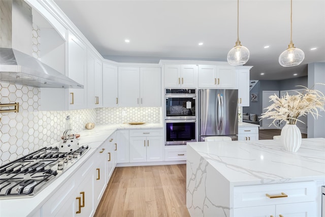 kitchen with white cabinetry, light stone counters, hanging light fixtures, appliances with stainless steel finishes, and wall chimney range hood