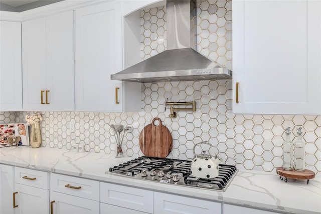 kitchen featuring white cabinets, stainless steel gas stovetop, light stone countertops, and wall chimney exhaust hood