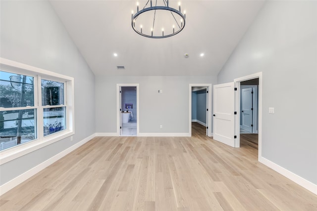 unfurnished living room with high vaulted ceiling, light hardwood / wood-style flooring, and a notable chandelier