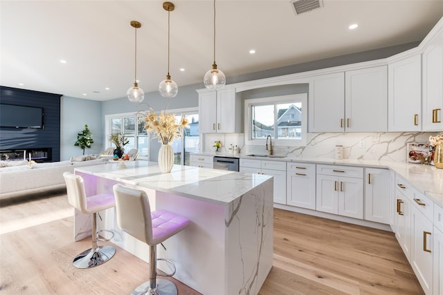 kitchen featuring sink, white cabinetry, pendant lighting, light stone countertops, and decorative backsplash