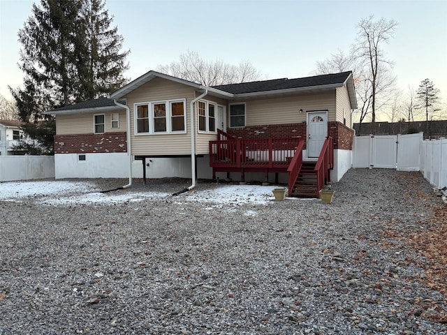 rear view of house with a wooden deck, brick siding, fence, and a gate