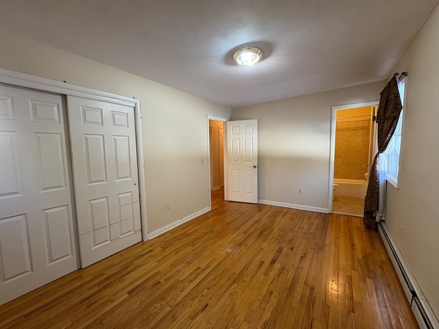 unfurnished bedroom with light wood finished floors, baseboards, baseboard heating, and a closet