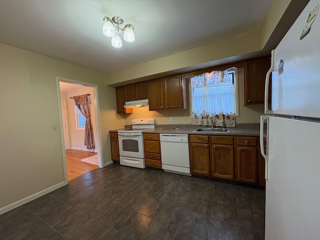 kitchen with white appliances, baseboards, dark countertops, under cabinet range hood, and a sink