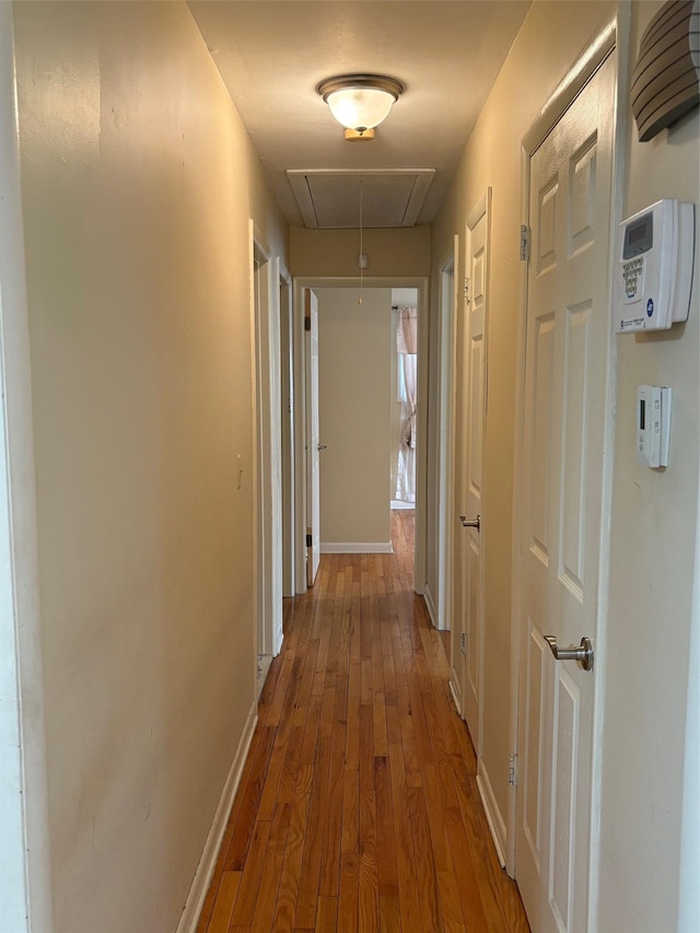 hallway featuring attic access, baseboards, and wood finished floors