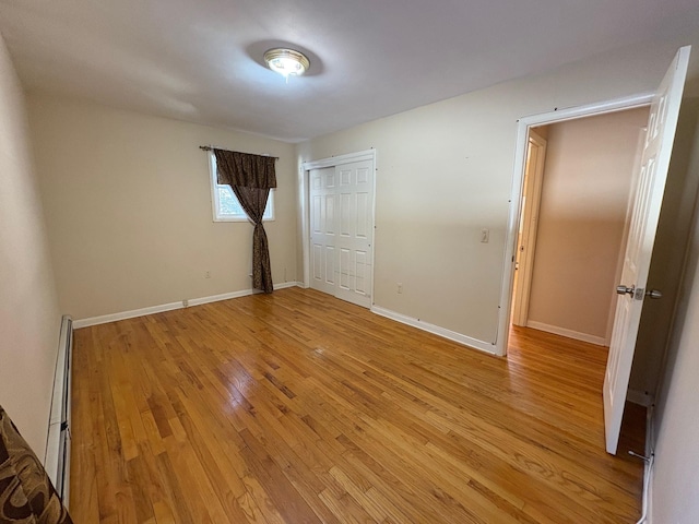 unfurnished bedroom with a closet, light wood-type flooring, a baseboard radiator, and baseboards